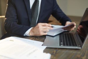Closeup portrait of unrecognizable successful businessman analyzing  contract documents at desk with laptop